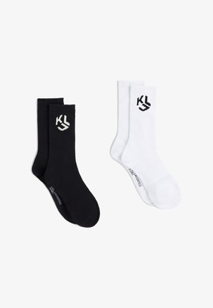 Due paia di calzini a coste alla caviglia, uno nero e uno bianco, ciascuno con il logo "KL" vicino alla parte superiore e un piccolo testo vicino alle dita.