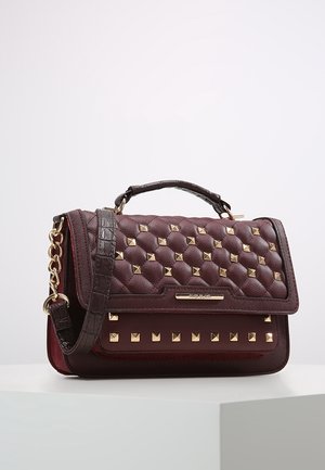 Ciemnobrązowa pikowana torebka z złotymi kwadratowymi ćwiekami, teksturowaną rączką oraz złotym łańcuszkowym paskiem, leżąca na białej powierzchni.