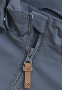 Gråstof med en glat tekstur har en lynlås og en tan lædertrækflap. Accentueret med et YKK lynlås brandskilt.