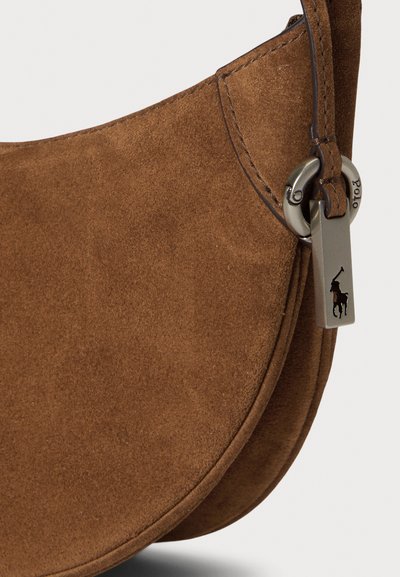 Brown suede crossbody bag with a curved shape. Features a metal logo tag and a smooth strap, highlighting the texture and clean lines.