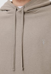 Sudadera beige con una tela texturizada, cordones ajustables y un pequeño logo de calavera de cabra bordado en el pecho.