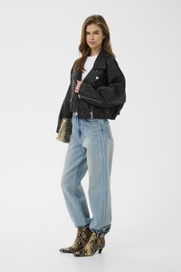 Jeune femme vêtue d'une veste en cuir noire, d'un haut blanc, d'un jean bleu clair et de bottines en cuir à motif serpent, tenant une pochette assortie en cuir à motif serpent.