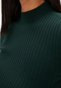 Maglione a coste di un verde scuro con design a collo alto, che mette in mostra un tessuto testurizzato e una silhouette aderente.