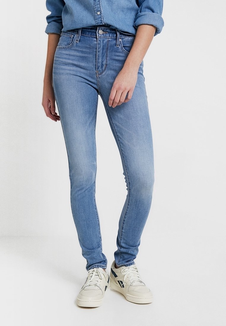 Jeans skinny de color azul claro, confeccionados en denim, con una cintura de altura media, un lavado descolorido y un diseño clásico de cinco bolsillos. Combinados con zapatillas blancas.