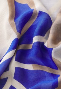 Écharpe en soie avec un motif géométrique en bleu profond, beige clair et blanc, offrant une texture douce et un tombé fluide.
