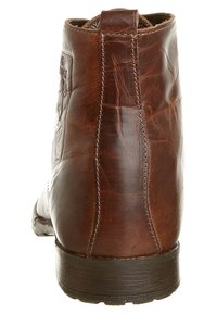 Stivaletto alla caviglia in pelle marrone con una texture liscia, punta arrotondata e cuciture visibili lungo il lato. Suola spessa in gomma scura.