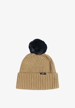 Beanie a coste color sabbia con un pompon in pelliccia sintetica nera sopra, dotato di una piccola etichetta nera con logo sul fronte.