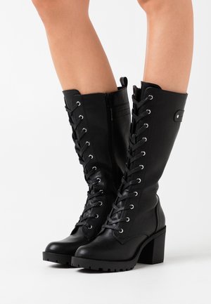 Black knee-high boots made of leather, featuring lace-up front, chunky block heels, and a side zipper for easy access. Textured grip sole.