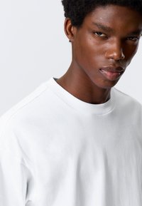 White cotton t-shirt featuring a round neckline and slightly loose fit, with visible stitching and a smooth, soft texture.