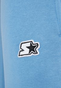 Ljusblått tyg med en mjuk textur som har en svart och vit broderad logotyp med en stjärna på sidan.