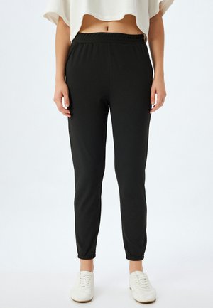 Sorte atletiske joggers med elastisk talje, tapered ben og manchetter. Stoffet er glat og strækbart, bæres med en cropped top og hvide sneakers.