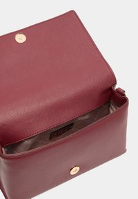 Bordeaux leren tas met een gestructureerd oppervlak, gouden hardware drukknoopsluiting en een gevoerde binnenkant met een logopatroon.