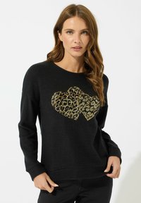 Svart tröja med ett hjärtformigt mönster i guld och leopardtryck i mitten. Mjuk textur, avslappnad passform med långa ärmar och ribbade muddar.