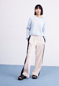 Light blue, textured sweater with “Jordan” logo; beige track pants with black side stripes; black slide sandals.