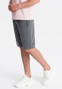 Grå bomulds shorts med sidelommer, elastisk talje og syet detalj, parret med hvide sneakers og en lys pink t-shirt.