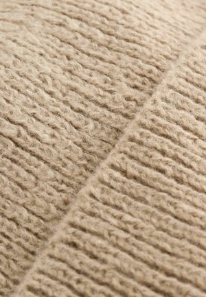 Textura țesăturii din lână tricotată în bej, cu modele alternante de nervuri și un aspect pufos, care arată fibre naturale moi și tonuri calde.