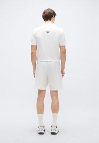 Biela polokošeľa s čiernym logom na chrbte, doplnená o rovnako ladené šortky. Ľahká tkanina, krátke rukávy a pohodlný strih.