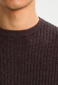 Pull en maille côtelée bordeaux foncé avec un col rond, présentant un motif texturé et une finition lisse. Vue en gros plan montrant les détails du tissu.