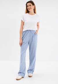 T-shirt bianca leggera con maniche arrotolate abbinata a pantaloni larghi a righe blu e bianche con vita elastica.