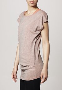 T-shirt rose clair à manches courtes en tissu doux et texturé avec un col rond et un dos légèrement plus long. Présente une doublure de col intérieur contrastante.