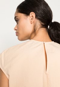 Top de cor pêssego com um acabamento texturizado, apresentando um design com recorte nas costas e mangas curtas, adequado para uso casual ou semi-formal.