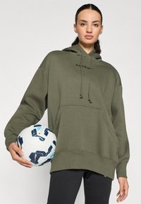 Sudadera verde oliva con un bolsillo frontal y cordones, presenta "PARÍS" impreso en negro. Una persona sostiene un balón de fútbol estampado.