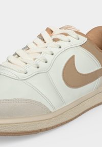 Бяла и бежова маратонка на Nike с връзки, завързани, показваща лого, пришито отстрани, и текстурирана подметка.