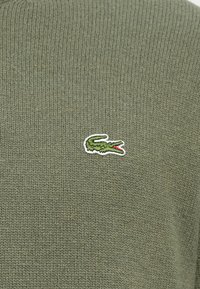 Zöld kötött anyag kis hímzett krokodil logóval, amelynek nyitott szája van, piros belsővel.