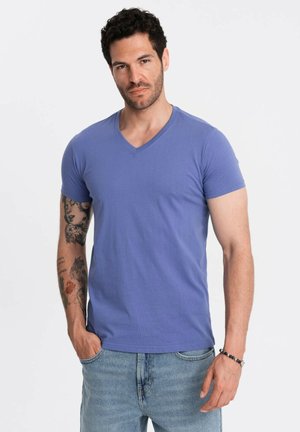 Camiseta de cuello en V y manga corta en azul claro, hecha de algodón, con un corte ajustado. El modelo lleva jeans desgastados de azul claro y accesorios.