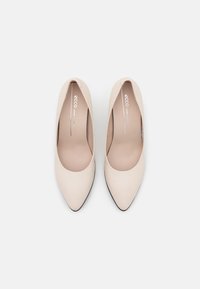 Escarpins à bout pointu en cuir beige au toucher lisse, au design décolleté et semelles noires. Le logo est visible sur la semelle intérieure.