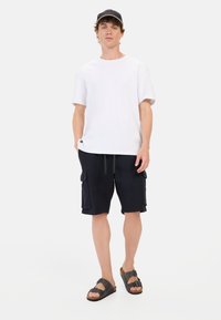 Witte t-shirt met korte mouwen gecombineerd met marineblauwe cargoshorts met zakken, en zwarte sandalen met verstelbare banden.