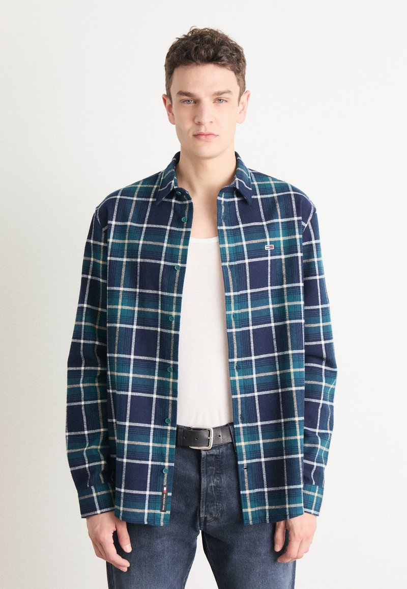 Camisa de franela a cuadros en azul marino y verde azulado, con líneas de rejilla blancas, diseño de botones y un pequeño logotipo en el bolsillo del pecho.