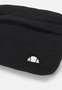 Funda acolchada negra con patrón de acolchado, que presenta un cierre de cremallera y un pequeño emblema bordado en beige y blanco en la esquina inferior.