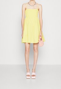 Gul sommarklänning med smockad bodice och spagettiband, A-linjär kjol. Kombination med rosa plattformssandaletter och matchande handväska.