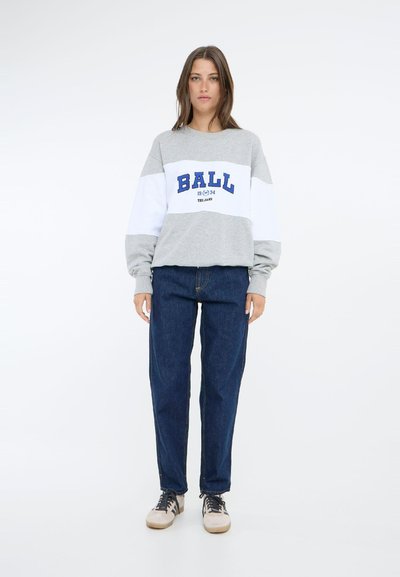 Grå hettegenser med hvite og blå detaljer, med teksten "BALL 1974". Kombinert med høyt liv mørke denimjeans og beige joggesko.