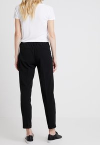 Pantalon noir fuselé avec taille élastique, détails de couture minimaux et revers, associé à un t-shirt blanc uni et des baskets noires.