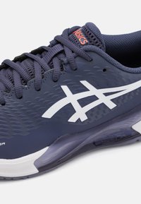 Asics sportska cipela u tamnoplavoj boji s bijelim detaljima, strukturiranom gornjom dijelu i zatvaranjem na vezanje. Sadrži umetke za gležnjeve i fleksibilnu potplat.
