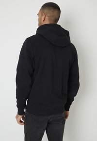 Sweat-shirt à capuche noir avec un tissu texturé, présentant une coupe décontractée, une poche kangourou et des poignets et un ourlet côtelés.