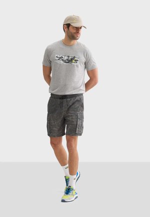 Grijze t-shirt met een grafische print, donkerbedrukte cargo shorts en kleurrijke hardloopschoenen met witte sokken. Verstelbare beige pet.
