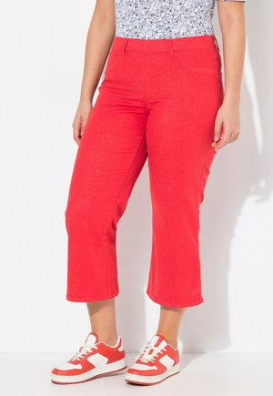 Rote, kurze Baumwollhosen mit Taschen, kombiniert mit rot-weißen Sneakers mit strukturierten Oberflächen und Schnürdesign.