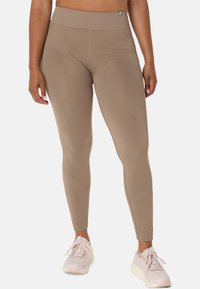 Tan high-waisted leggings with a ribbed texture, featuring subtle patterns and a sleek, form-fitting design. Paired with light sneakers.