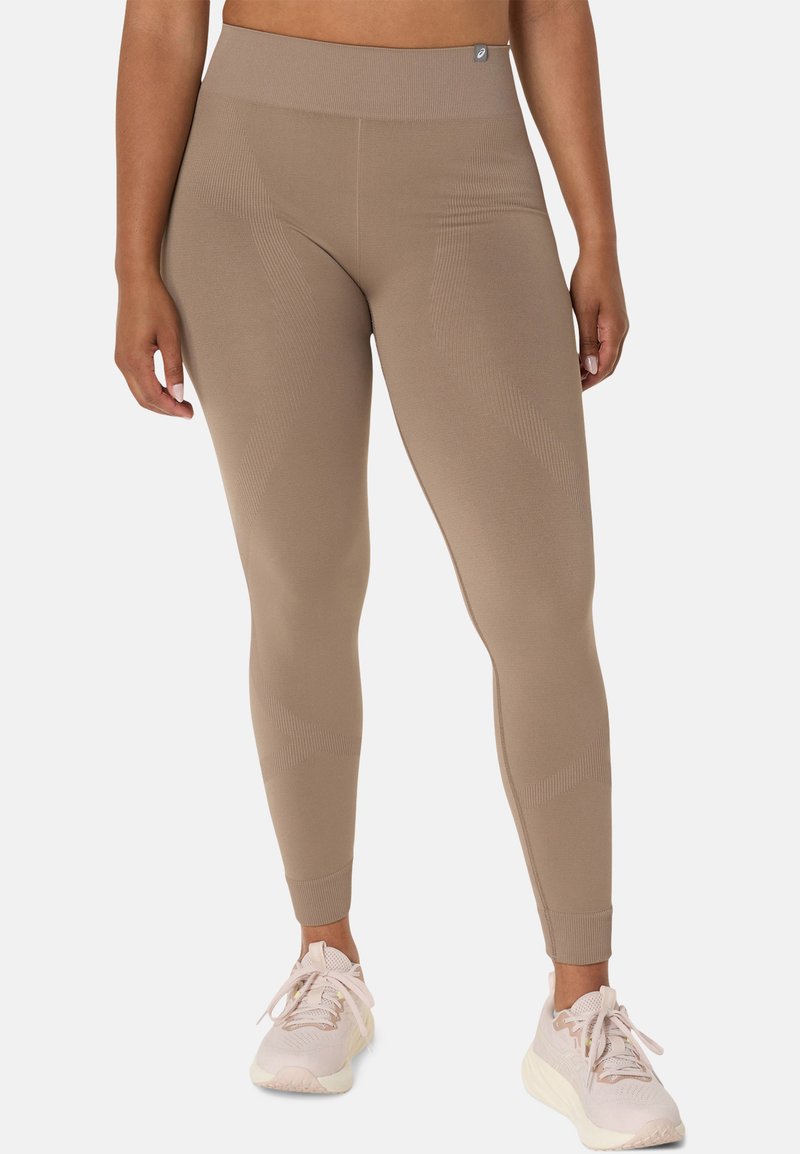 Tan high-waisted leggings with a ribbed texture, featuring subtle patterns and a sleek, form-fitting design. Paired with light sneakers.