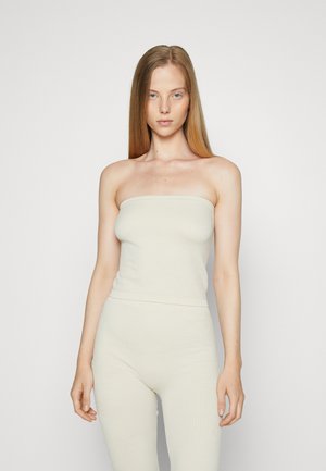 Gaiši bež strapless tops ar teksturētu virsmu, saskaņots ar pieguļošām biksēm. Abiem apģērba gabaliem ir bezšuvju dizains un minimāls apdare.