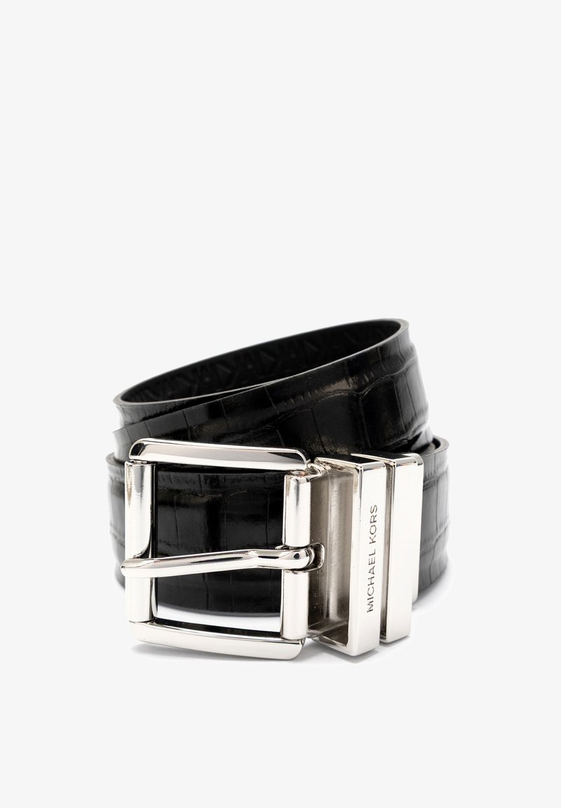 Ceinture en cuir noir à motif crocodile enroulée avec une boucle rectangulaire en argent et un fermoir métallique gravé "MICHAEL KORS" sur fond blanc.
