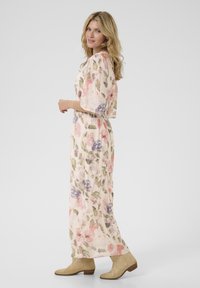 Rochie lungă, florală, cu mâneci largi; culori pastelate cu flori roz, mov și verzi pe un fundal deschis. Botine din suede până la gleznă.