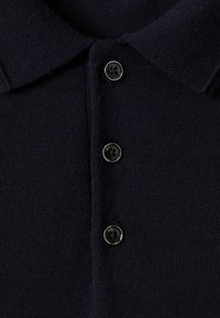 Tricou polo bleu închis dintr-un material texturat, având guler deschis și patru butoane negre cu un design floral pe fiecare.