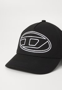 Casquette de baseball noire avec un design structuré, présentant un logo brodé blanc et des détails de couture sur la visière. Forme de couronne ronde.