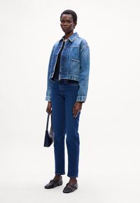 Giacca in denim con chiusura a bottoni, colore azzurro chiaro, e tasca sul petto, abbinata a jeans dritti blu scuro e ballerine nere a punta.