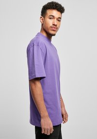 Tricou din bumbac violet, cu mâneci scurte și decolteu cu guler rotund, prezentat pe un model pe un fundal neutru, având o croială lejeră.