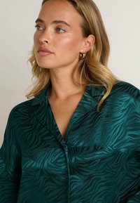 Chemise vert émeraude avec un motif de rayures zébrées subtil, en matériau soyeux, dotée d'un col et d'une fermeture à boutons.